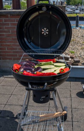 Black Compact Charcoal Grill Kettle with Fried Vegetables Stay on the Terrace, in garden or on the Roof Top.