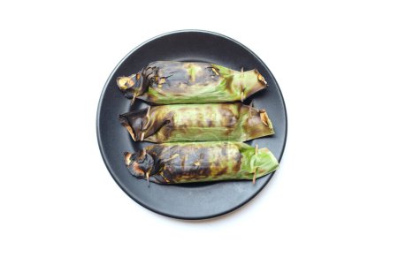 Foto de Comida tradicional de Tailandia hecha de arroz pegajoso envuelto en hojas de plátano con taro y relleno de plátano y a la parrilla en un plato de cerámica negra - Imagen libre de derechos