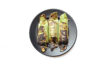 Foto de Comida tradicional de Tailandia hecha de arroz pegajoso envuelto en hojas de plátano con taro y relleno de plátano y a la parrilla en un plato de cerámica negra - Imagen libre de derechos