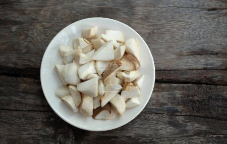 Téléchargez les photos : Émincés de champignons d'huîtres royales crues et rosmary (Pleurotus eryngii) dans une assiette blanche isolée sur un fond en bois, préparer la nourriture - en image libre de droit