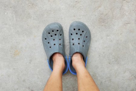Bein Frau und Paar blaue Holzschuhe isoliert auf dem Zement. Sommer-Aqua-Schuhe mit Löchern und Riemen an der Ferse Silikonschiefer . 