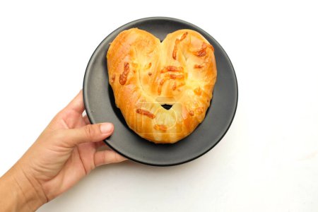 Téléchargez les photos : Main de femme tenant une délicieuse maison un pain fraîchement cuit boulangerie en forme de coeur, bretzels doux, pain danois dans une plaque blanche isoler sur un fond blanc. pour Valentine. Idéal pour les amoureux - en image libre de droit