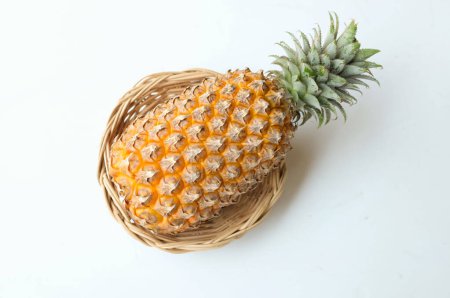 Téléchargez les photos : Frais un ananas (ananas comosus (l.) merr) jaune mûr biologique dans un panier de bambou isoler sur une toile de fond blanche. concept de fruits d'été. - en image libre de droit
