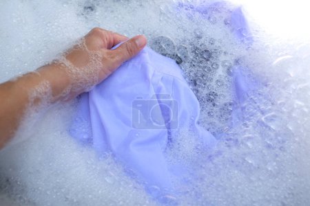Mano de ama de casa asiática lavando ropa blanca, uniforme escolar, uniformes de estudiante con detergente de burbujas en el lavabo.