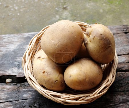 Téléchargez les photos : Tas de pommes de terre fraîches crues pour bébés (Solanum tuberosum) ou pommes de terre jeunes dans un panier en osier sur une table en bois - en image libre de droit