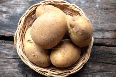Téléchargez les photos : Tas de pommes de terre fraîches crues pour bébés (Solanum tuberosum) ou pommes de terre jeunes dans un panier en osier sur une table en bois - en image libre de droit