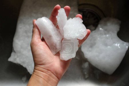 human hand holds Ice crystals fromfreezer in refrigerator
