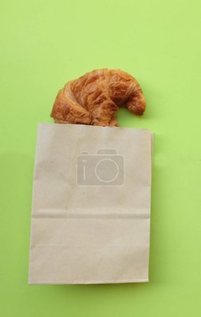 Foto de Deliciosos croissants deliciosos recién horneados en una bolsa de papel marrón sobre un fondo verde con golosinas dulces, vista superior. concepto minimalista - Imagen libre de derechos