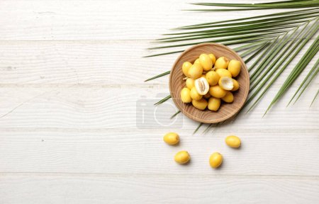 Téléchargez les photos : Groupe de fruits jaunes de palmier phénix dactylifera ou de palmier dattier dans une assiette circulaire en bois isolé sur le fond de table en bois blanc.Alimentation saine, Ramadan traditionnel, délicieux et sain - en image libre de droit