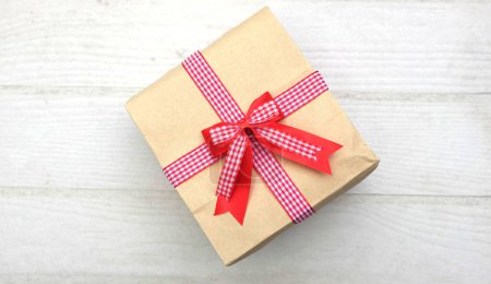 Téléchargez les photos : Vue d'en haut ofgirl mains asiatiques en chandail coloré tenant boîte cadeau en papier artisanal avec ruban rouge arc sur une table en bois blanc. - en image libre de droit