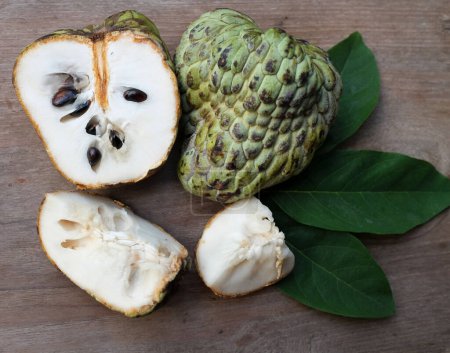 fresh green raw custard apple,sugar apple, annona cherimola (annona squamosa l.) fruit  cut in half sliced with leaves isolated on a wooden table tropical exotic fruit and healthy fruits