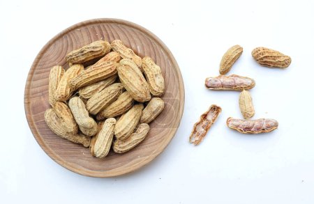Téléchargez les photos : Tas d'arachides bouillies, arachides, noix, arachides non pelées et pelées dans une assiette en bois isolé sur fond blanc. vue du haut.flatlay - en image libre de droit