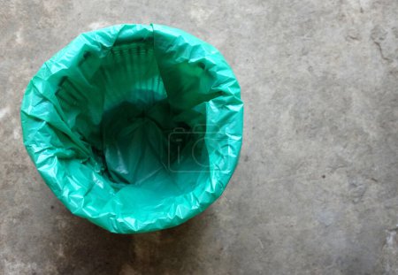 Mülleimer mit grünen Plastiktüten isoliert auf dem Zementboden Hintergrund. Symbol für Abfallwirtschaft und Umwelt