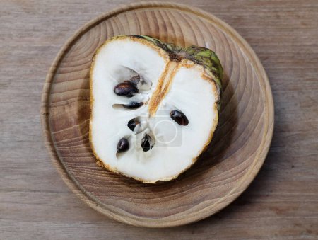 fresh green raw custard apple,sugar apple, annona cherimola (annona squamosa l.) fruit cut in half sliced in a wooden plate isolated on a wooden table. tropical exotic fruit and healthy fruits