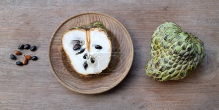 fresh green raw custard apple,sugar apple, annona cherimola (annona squamosa l.) fruit cut in half sliced in a wooden plate isolated on a wooden table. tropical exotic fruit and healthy fruits