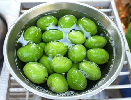 frische grüne rohe Bio-Mangos (Mangifera indica L. Var.) Obst in einer Schüssel mit Wasser auf dem Tisch.Konservierungskonzept Obst lange haltbar machen, Fruchtkompott, Mangos einlegen 