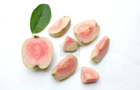 Foto de Guayaba rosada madura dulce, guayaba roja (psidium guajava) fruta con hojas verdes y medias rebanadas, entera aislada sobre fondo blanco, vista superior, puesta plana, concepto de fruta saludable - Imagen libre de derechos
