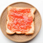 a bird's eye view of the raspberry strawberry jam, fresh red berries spread on slice of bread on a wooden plate isolate on a white backdrop. Healthy snack and food ideas
