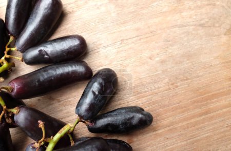 Bunch of fresh Sweet black seedless Moon Drops grape,Purple Witch Finger grapes,Sapphire Grapes or Witch Fingers grape isolated on a wooden table backdrop.black grapes. Grapes black taste sweet growing nature