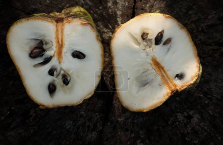 fresh green raw custard apple,sugar apple, annona cherimola (annona squamosa l.) fruit cut in half sliced with leaves on a wooden backdrop. tropical exotic fruit and health