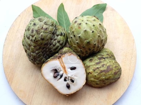 fresh green raw custard apple,sugar apple, annona cherimola (annona squamosa l.) fruit cut in half sliced with leaves on a wooden cutting board  backdrop. tropical exotic fruit and health