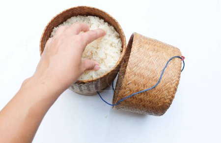 Mujer de mano asiática recogiendo arroz caliente tailandés pegajoso al vapor en caja de estilo tradicional de bambú de madera sobre arroz glutinoso de fondo blanco. Un alimento básico popular en Tailandia