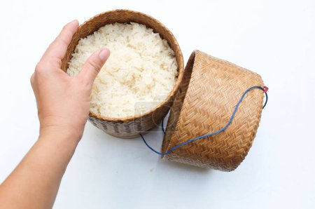 Mujer de mano asiática recogiendo arroz caliente tailandés pegajoso al vapor en caja de estilo tradicional de bambú de madera sobre arroz glutinoso de fondo blanco. Un alimento básico popular en Tailandia