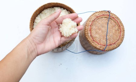 Eine asiatische Hand nimmt warmen gedämpften thailändischen klebrigen Reis in einer traditionellen Bambusbox auf weißem Hintergrund auf. Ein beliebtes Grundnahrungsmittel in Thailand