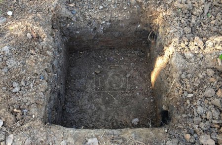 Dig a hole for placing the concrete pillar.Dug out rectangular pit. Close-up Texture.square shaped hole into the middle of the lawn.