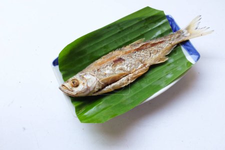 Vue de dessus d'une délicieuse carpe frite (Barbonymus gonionotus) sur une assiette servie avec des feuilles de banane vertes isolées sur fond blanc. Célèbre menu de poisson frit dans le restaurant thaïlandais