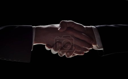 Photo for Photo of two men in suits shaking hands on a black background - Royalty Free Image