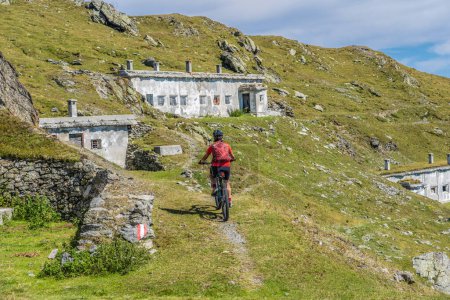 Foto de Mujer mayor agradable y activa que monta su bicicleta de montaña eléctrica en una vieja carretera militar de Toblach upt a la cumbre de Marchkinkele con vista espectacular a los tres picos de Lavaredo, Tirol del Sur, - Imagen libre de derechos