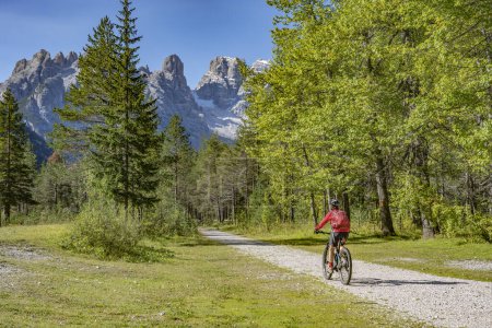 Foto de Mujer mayor agradable y activa montar su bicicleta de montaña eléctrica en un antiguo terraplén ferroviario en el valle de Hoehlenstein entre Toblach y Cortina Dampezzo, Tres picos Dolomitas, Tirol del Sur, Italia - Imagen libre de derechos