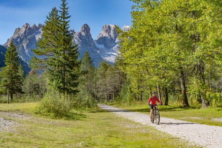 Téléchargez les photos : Belle et active femme âgée chevauchant son vélo de montagne électrique sur un vieux remblai ferroviaire dans la vallée Hoehlenstein entre Toblach et Cortina Dampezzo, Trois pics Dolomites, Tyrol du Sud, Italie - en image libre de droit