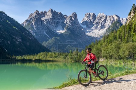 Foto de Mujer mayor agradable y activa que monta su bicicleta de montaña eléctrica en el lago Duerrenstein en el valle de Hoehlenstein entre Toblach y Cortina Dampezzo, Dolomitas de Three Peaks, Tirol del Sur, Italia - Imagen libre de derechos