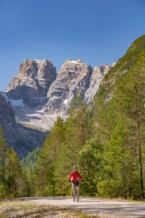 Photo for Nice and active senior woman riding her electric mountain bike on an old railway embankment in the Hoehlenstein valley  between Toblach and Cortina Dampezzo, Three Peaks Dolomites, South Tirol, Italy - Royalty Free Image