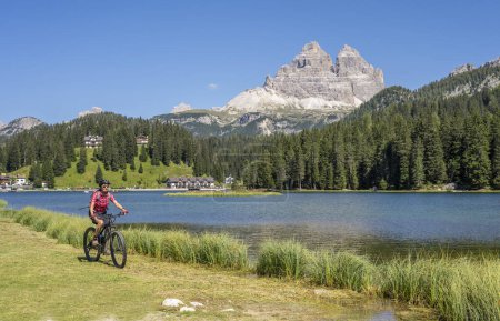 Photo for Nice senior woman ridung her electric mountain bike at the shore of Misurina Lake below the famous summits of the Three peak of Lavaredo in the Dolomites mountains in South Tirol, Italy - Royalty Free Image