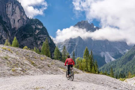 Foto de Bonita mujer mayor montando su bicicleta de montaña eléctrica en el valle de Innerfeld en los Dolomitas Sexten cerca de la aldea de Innichen, Parque Nacional de Tre cime, Tirol del Sur, Italia - Imagen libre de derechos
