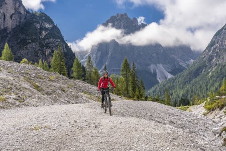 Photo for Pretty senior woman riding her electric mountainbike in the Innerfeld Valley in the Sexten Dolomites near village of Innichen , Tre cime National park, South Tirol, Italy - Royalty Free Image