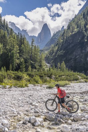 Foto de Bonita mujer mayor montando su bicicleta de montaña eléctrica en el valle de Fischlein en el Sexten Dolomites ingenio famoso Sextan reloj de sol en el fondo, Parque Nacional de Tre cime, Tirol del Sur, Italia - Imagen libre de derechos