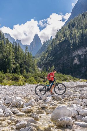 Foto de Bonita mujer mayor montando su bicicleta de montaña eléctrica en el valle de Fischlein en el Sexten Dolomites ingenio famoso Sextan reloj de sol en el fondo, Parque Nacional de Tre cime, Tirol del Sur, Italia - Imagen libre de derechos