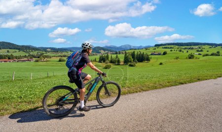 pretty senior woman riding her electric mountain bike and enjoying the spectacular view over the Allgau and Bregenz Forest alps near Steibis, Bavaria, Germany
