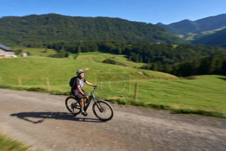 Photo for Pretty senior woman riding her electric mountain bike and enjoying the spectacular view over the Allgau and Bregenz Forest alps near Steibis, Bavaria, Germany - Royalty Free Image