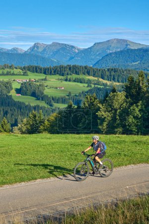 Téléchargez les photos : Jolie femme âgée en VTT électrique et profitant de la vue spectaculaire sur les Alpes Allgau et Bregenz près de Steibis, Bavière, Allemagne - en image libre de droit