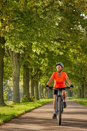 attractive senior woman cycling with her electric mountain bike in an old avenue in Ludwigsburg, Baden-Wuerttemberg, Germany 