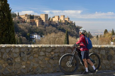 Foto de Bonita mujer mayor activa en bicicleta con su bicicleta de montaña eléctrica en Granada por debajo del Patrimonio de la Humanidad de Alhambra, Granada, Andalucía, España, - Imagen libre de derechos