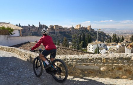 nice active senior woman cycling with her electric mountain bike in Granada below the world heritage site of Alhambra, Granada, Andalusia,  Spain,