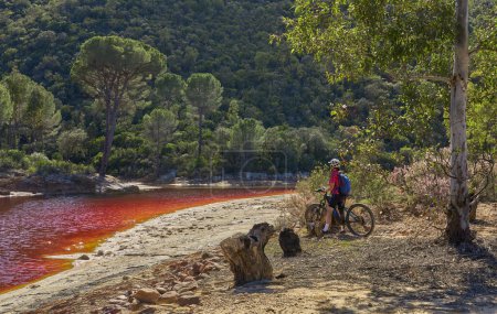 Téléchargez les photos : Belle femme avec vélo de montagne électrique lors d'un tour à vélo le long de la rivière Rio Tinto avec son eau rouge naturelle en Andalousie, Espagne - en image libre de droit