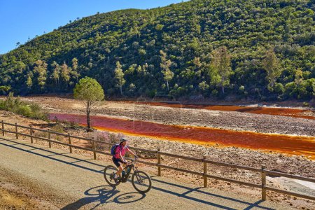 Foto de Agradable mujer con bicicleta eléctrica en un recorrido en bicicleta a lo largo del río Tinto con su agua roja natural en Andalucía, España - Imagen libre de derechos