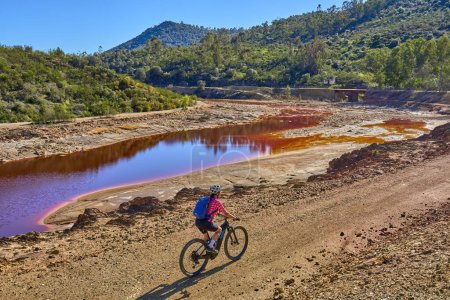 nice woman with electric moutain bike on a bike tour along river Rio Tinto with its natural red water in Andalusia, Spain